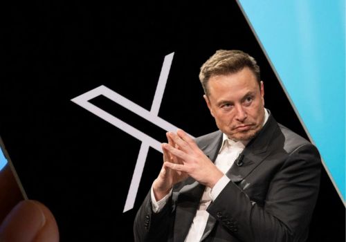 Elon Musk sitting in front of X logo